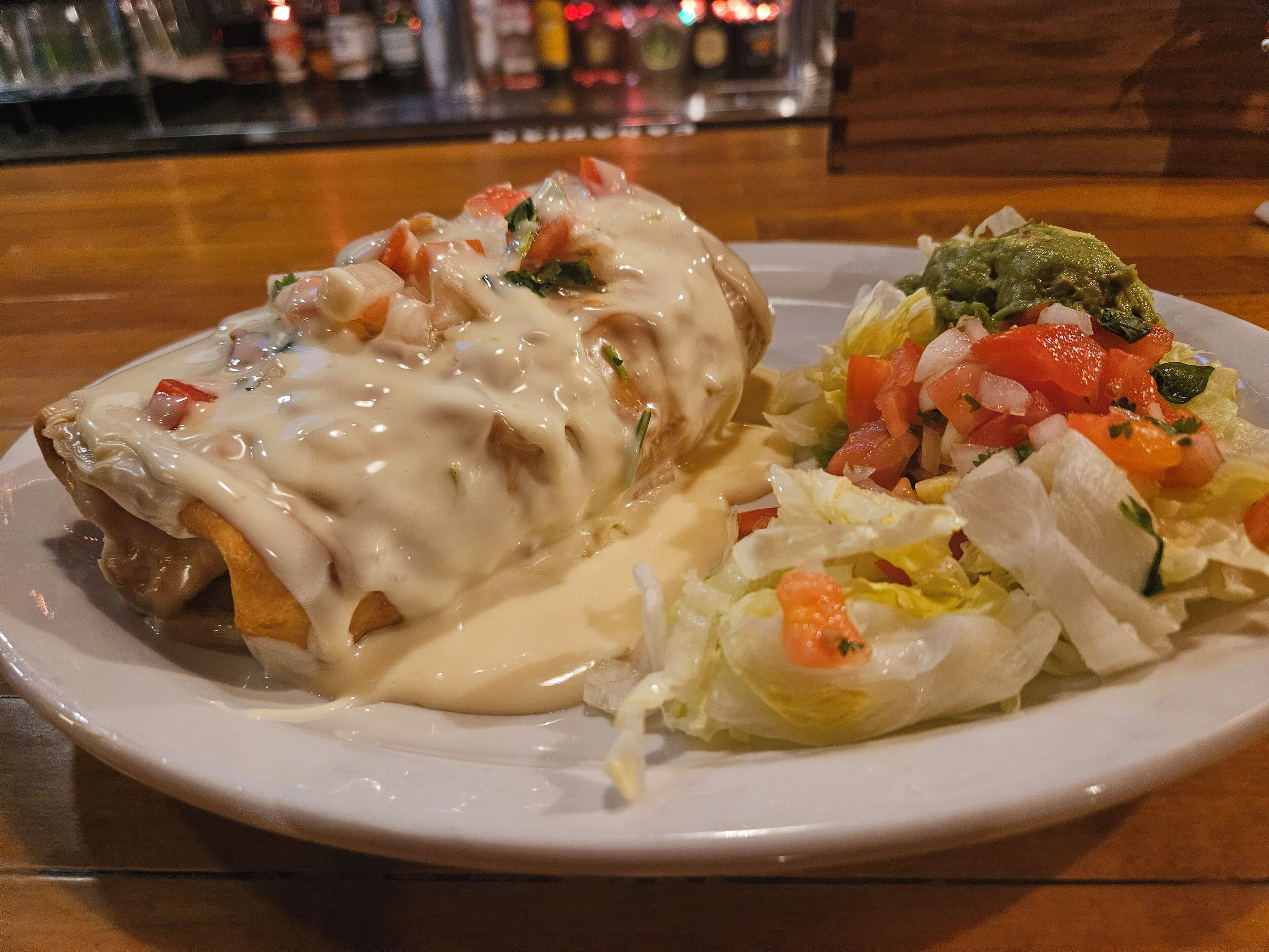 Un plato con un alimento empanizado, salsa cremosa y una ensalada con tomates y lechuga.