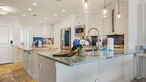 A modern kitchen with white cabinetry, a central island, stainless steel appliances, and pendant lighting. - La Mer on 10th - A Luxurious holiday stay! (St. Augustine Beach)