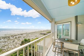 Un balcon avec vue sur la plage, une table avec des chaises et un luminaire suspendu.