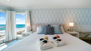 A hotel room with a large bed, two bedside tables, a view of the beach, and a patterned wallpaper. - La Mer on 10th - A Luxurious holiday stay! (St. Augustine Beach)