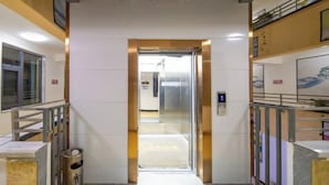 A hotel corridor with a modern elevator, glass doors, and a metal railing. - Nanyou Hotel Lijiang Wangjiang Business Hotel (Lijiang)