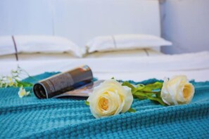 Ein Bett mit weißen Leinentüchern, einer blauen Strickdecke und zwei weißen Rosen darauf.