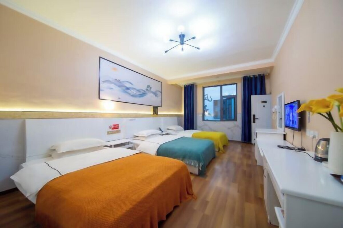 Hotellihuone, jossa on kolme sänkyä, työpöytä, televisio ja ikkuna, jossa on verhot.