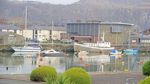 Un port de plaisance où sont amarrés plusieurs bateaux, un bâtiment en pierre et un paysage montagneux en arrière-plan.