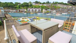 Une terrasse dotée de meubles en osier et d’une table, offrant une vue sur une marina avec des bateaux et des maisons en arrière-plan.