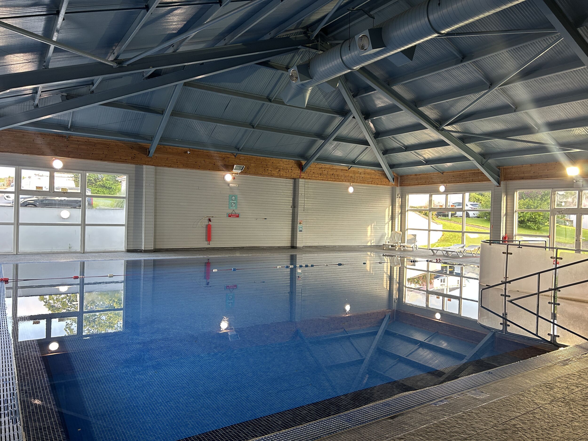 Una piscina interior amb una vista clara de la zona de la piscina, equips de seguretat i una finestra gran que ofereix una vista de l'exterior.