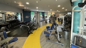 Uma academia com diversos equipamentos de ginástica, uma pista de corrida amarela e espelhos nas paredes.