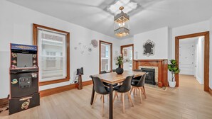A dining area with a wooden table and chairs, a jukebox, and a fireplace. - 7bdrm, 3baths, 2 kitchens, mins to falls, Arcade, WiFi, AC, parking (Niagara Falls)