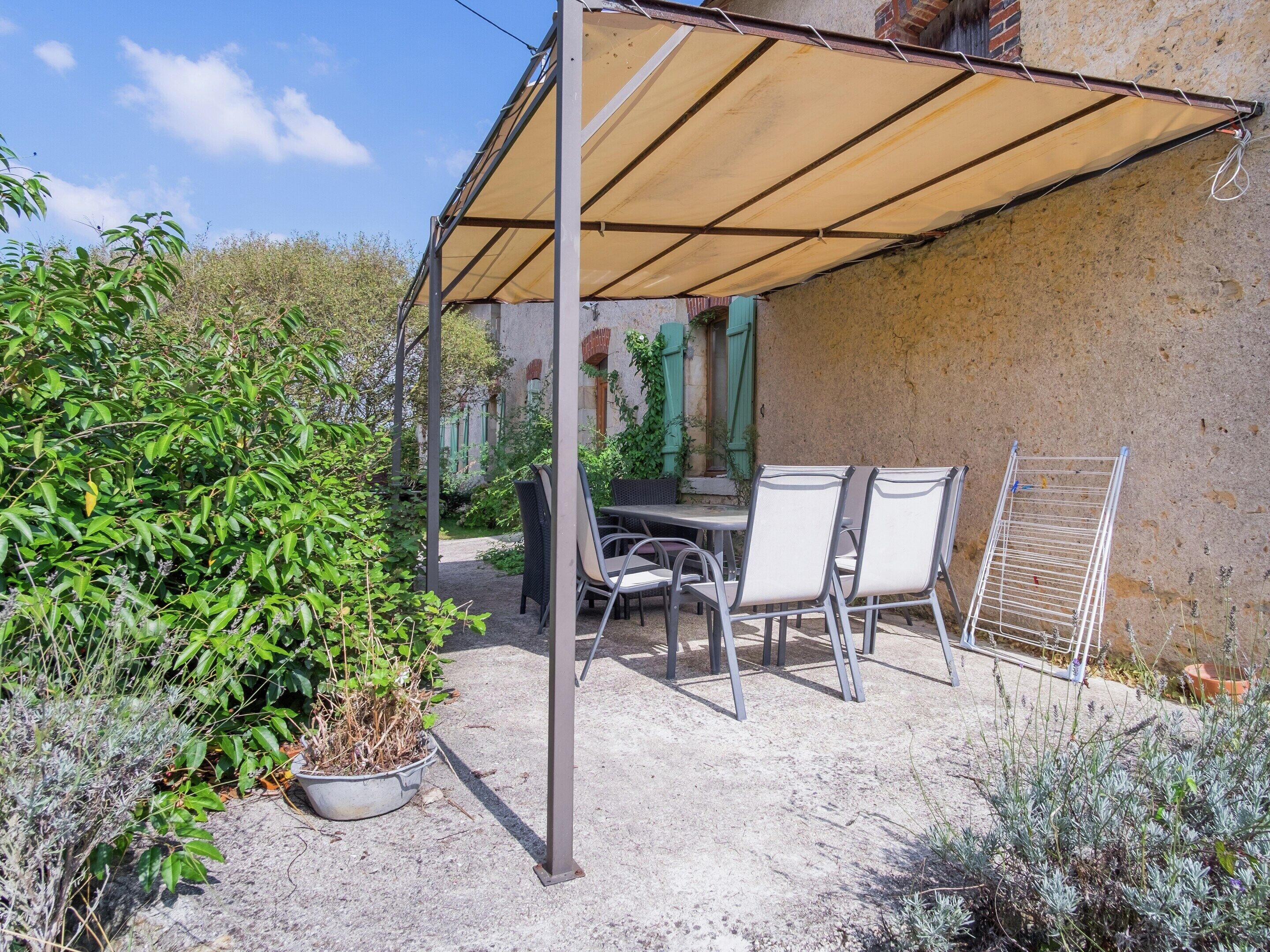 Patio esterno con tavolo e sedie, circondato da piante e un pergolato.