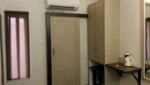 Una habitación de hotel compacta con una cama individual, una mesita pequeña, una silla, un equipo de aire acondicionado y un armario.