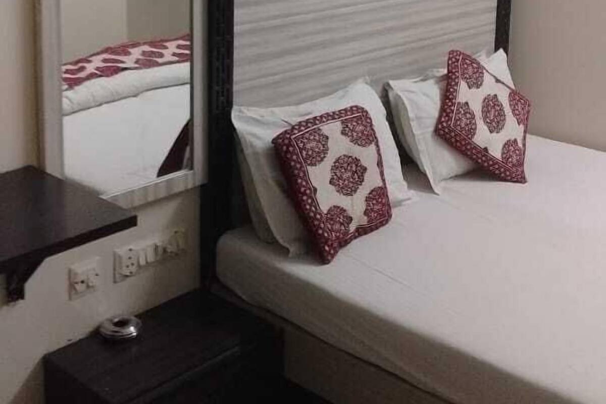 A bedroom with a bed, a nightstand, a mirror, and a wall-mounted shelf.