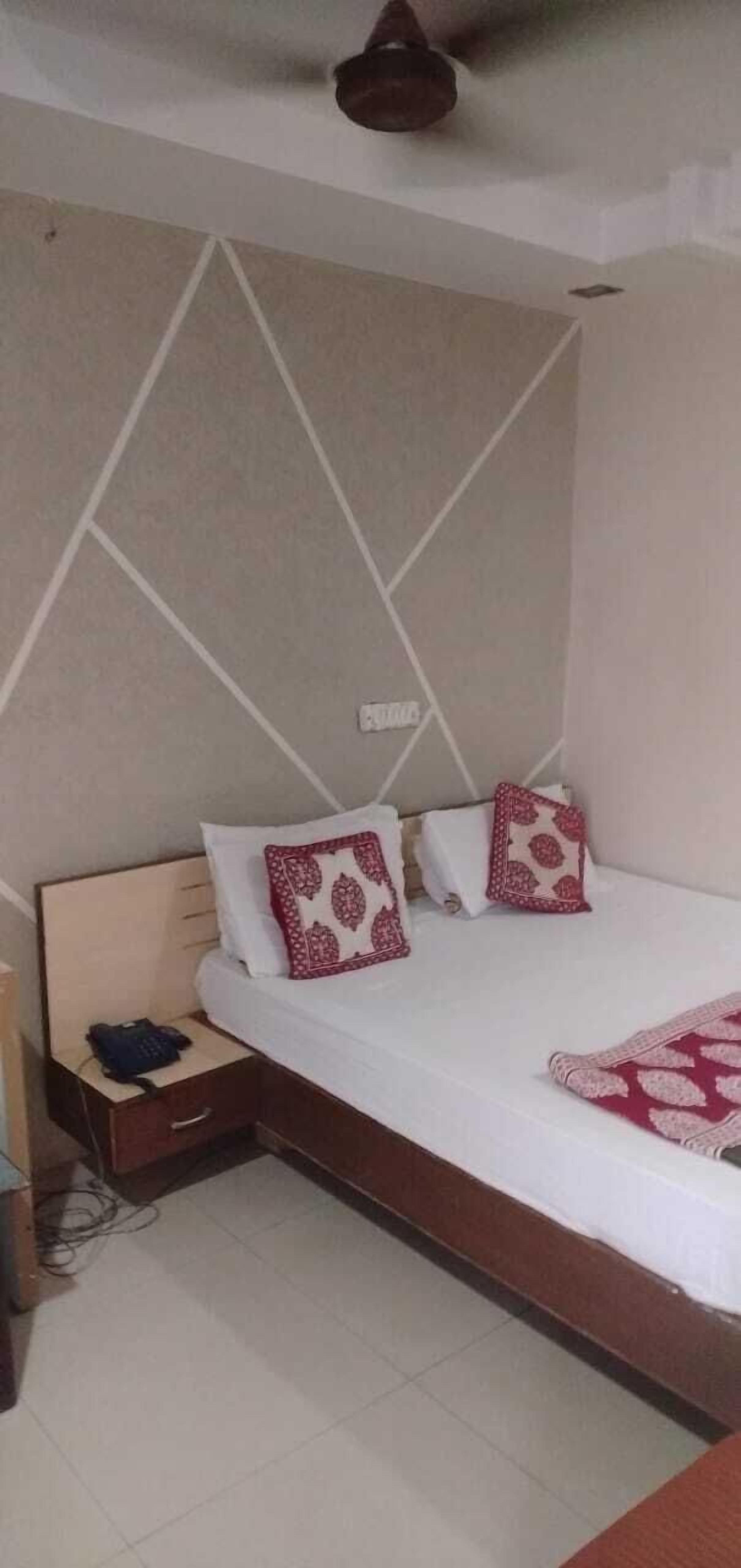 Cama bem arrumada com almofadas estampadas, mesa de cabeceira com telefone e parede com design geométrico.