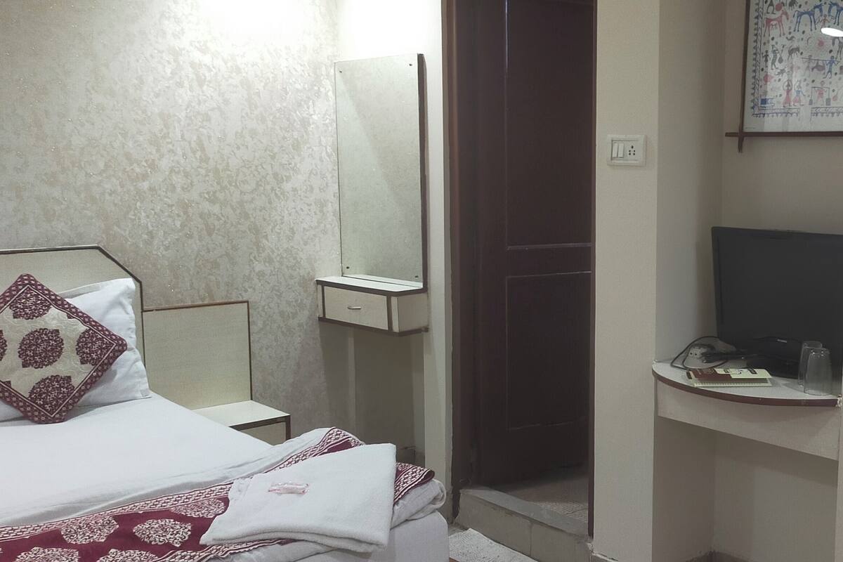 A hotel room with a bed, a bedside table, a mirror, a small desk, and a window with a view.