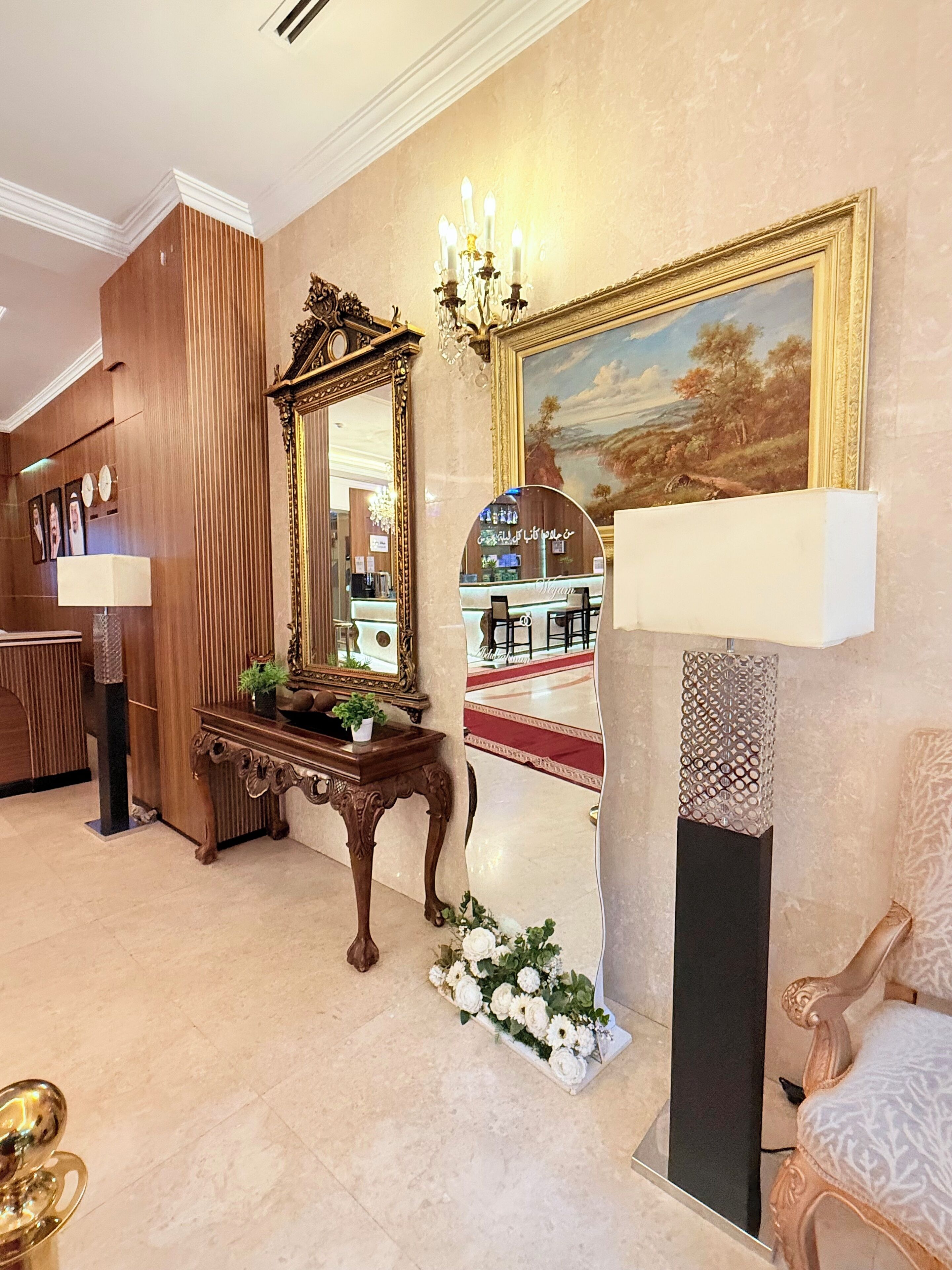 A lobby with a wooden reception desk, a large mirror, a chandelier, a painting, and a patterned wall.