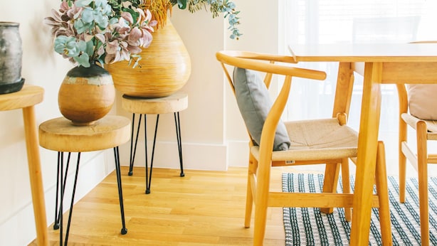 Una mesa de madera con sillas, un florero con flores y una estantería con objetos decorativos.