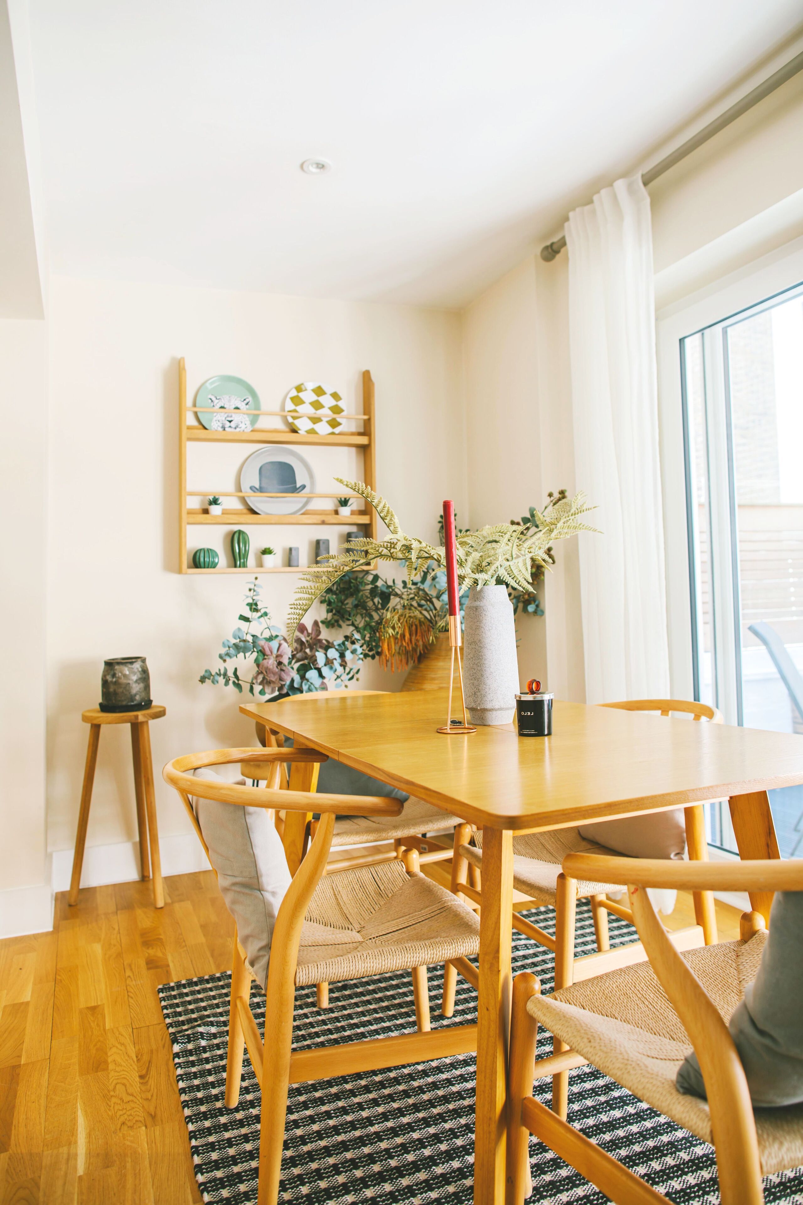 Un comedor con una mesa y sillas de madera, una mesita auxiliar, un florero con una planta y un estante con adornos.