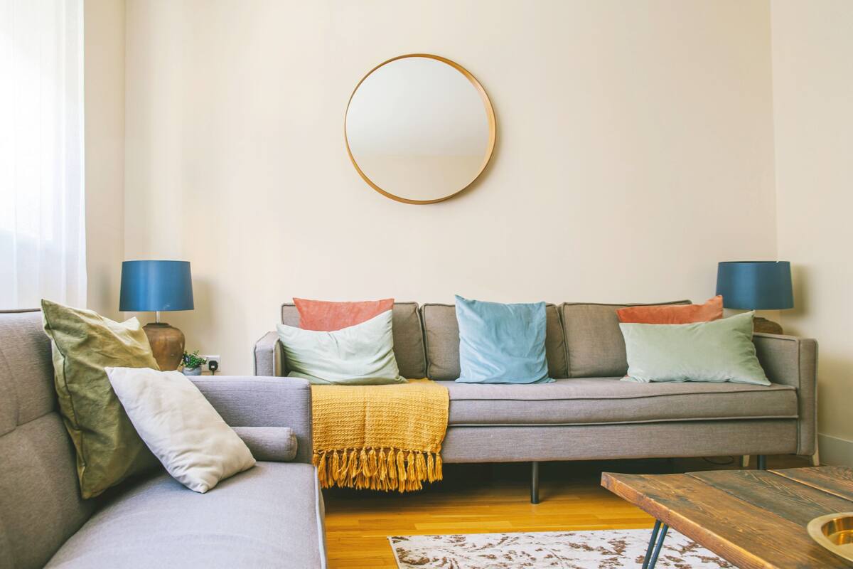 A living room with a grey sofa, a round mirror, and two lamps.