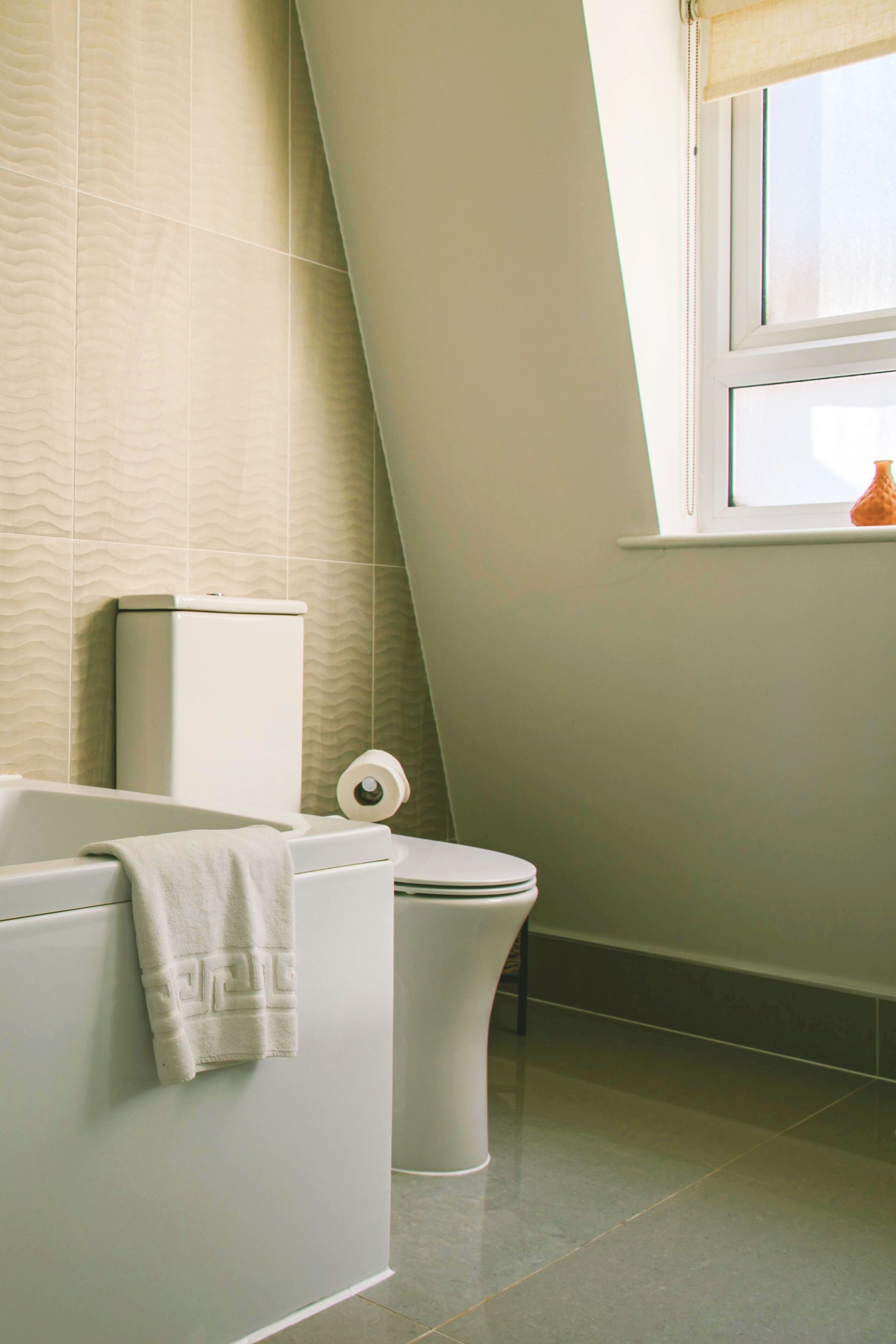 A modern bathroom with a toilet, a bathtub, and a window with a curtain.