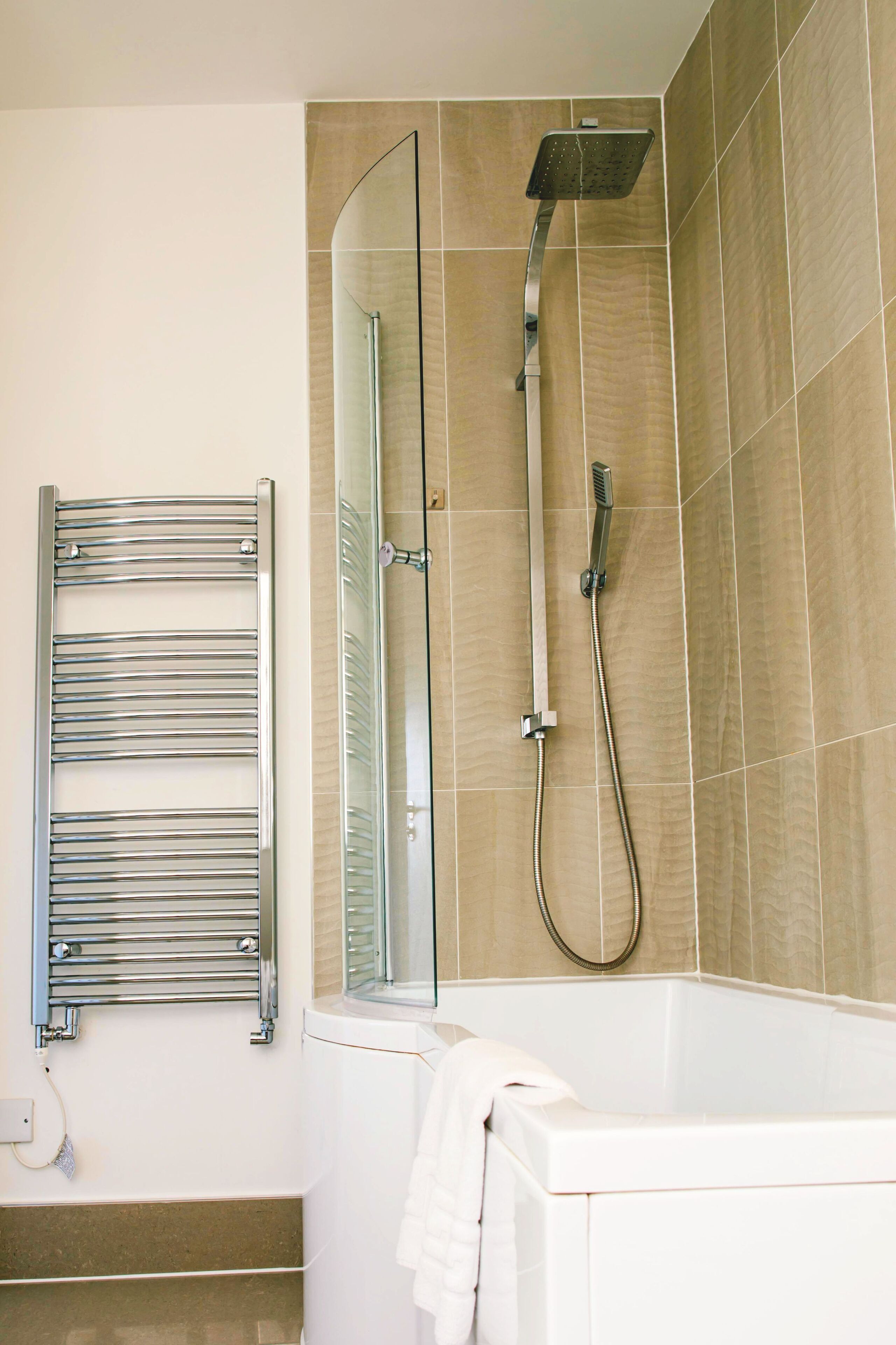 A modern bathroom with a glass-enclosed shower, a white bathtub, and a chrome towel rack.