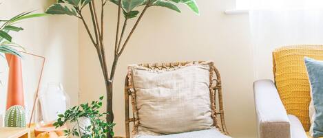 A cozy living room with a large potted plant, a wicker chair, a small ottoman, and a yellow armchair.