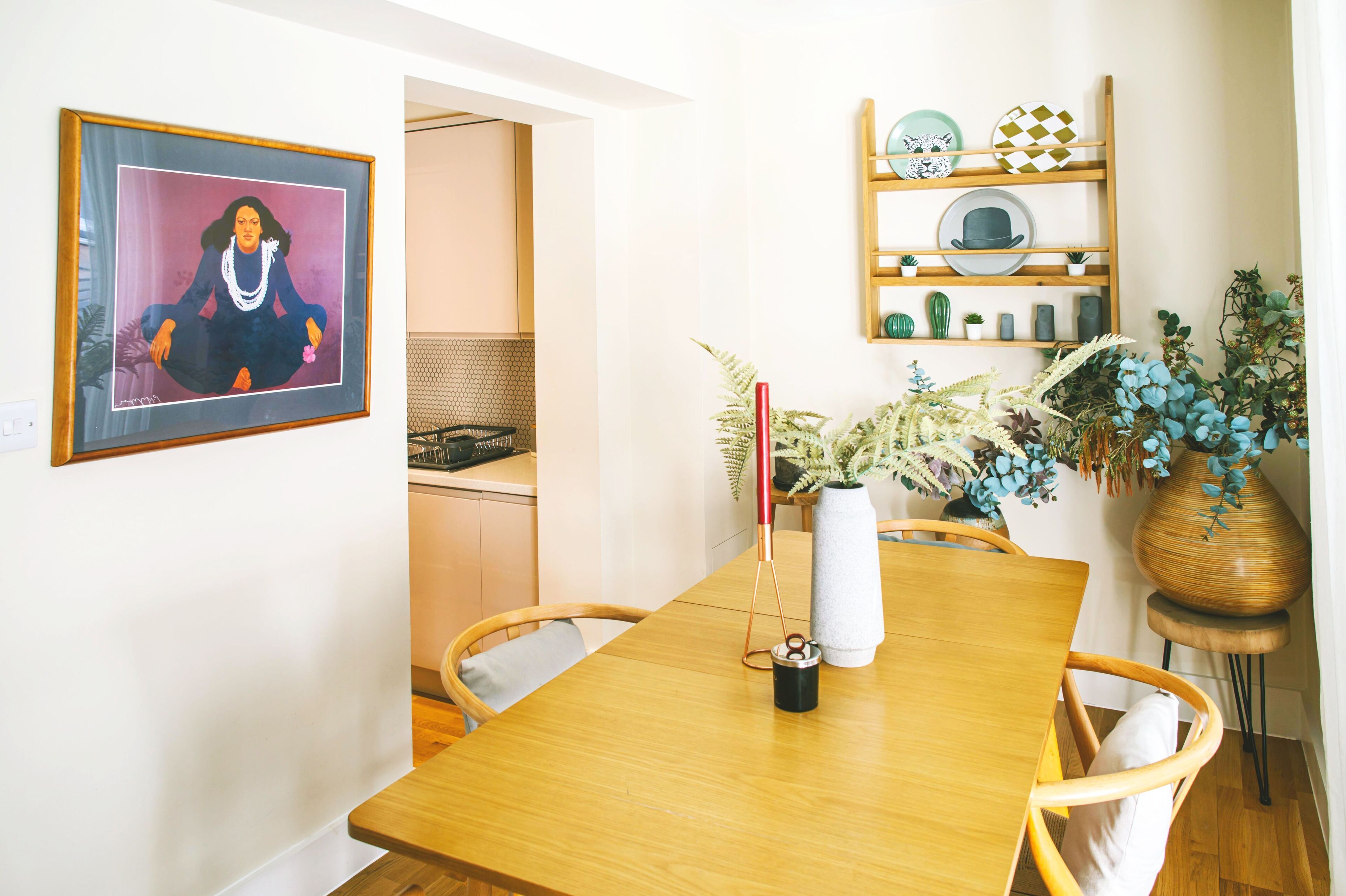 Un coin repas comprenant une table en bois, des chaises, un vase avec des fleurs, un tableau encadré et une étagère avec des objets décoratifs.