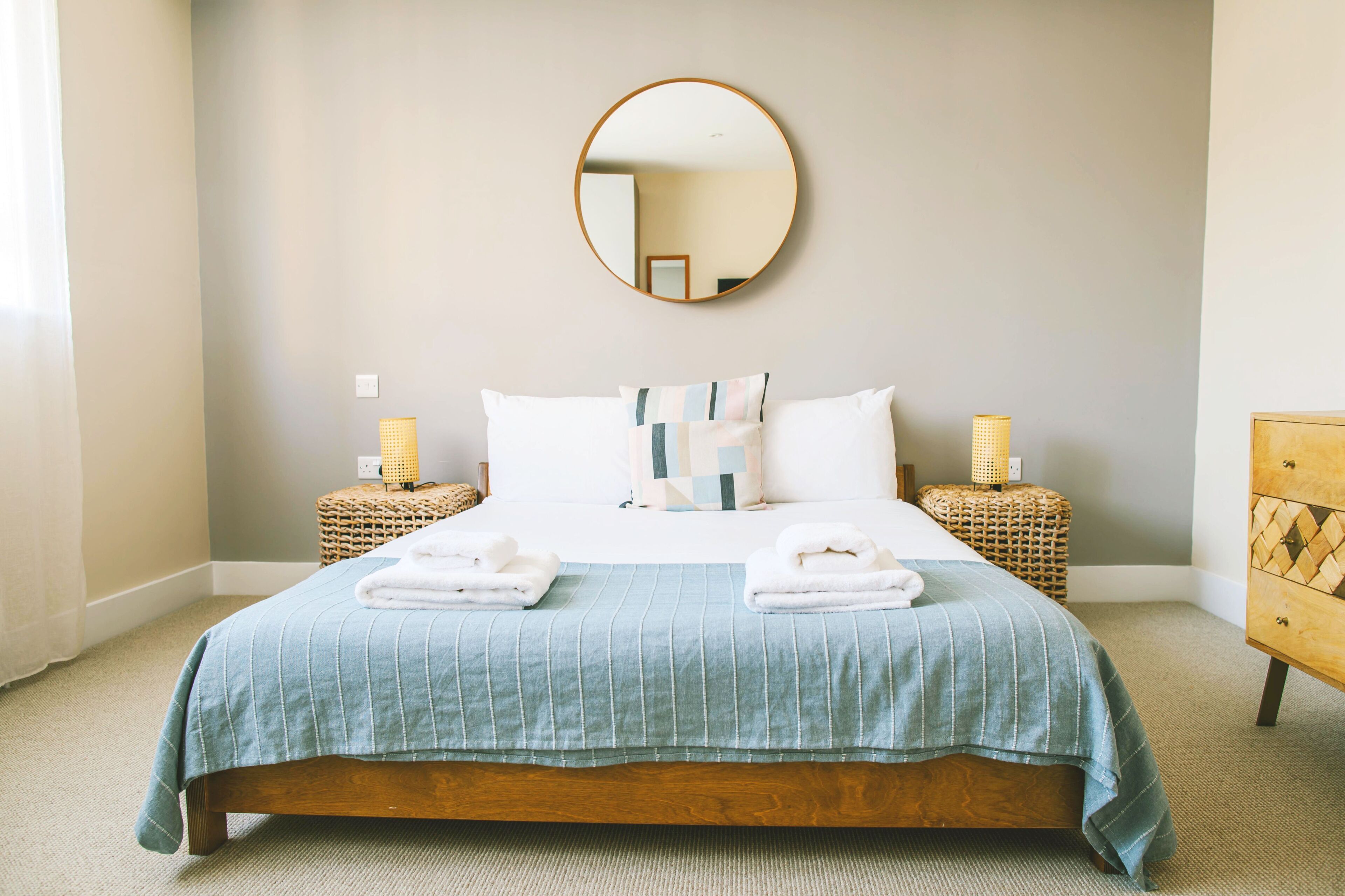 A neatly made bed with a blue bedspread and white pillows, flanked by two wicker nightstands with lamps.