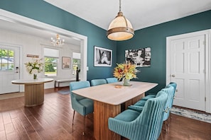 Un espace repas comprenant une table en bois, des chaises recouvertes d’un tissu turquoise et un luminaire suspendu.