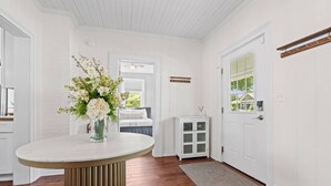 A room with a white door, a white cabinet, a round table with a vase of flowers, and a bench with a view. - Chestnut Estate: 2 Homes · Hot Tub + Fire Pit (Douglas)