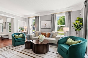 Un salon comprenant un canapé, deux fauteuils, une table basse et de grandes fenêtres avec des rideaux.