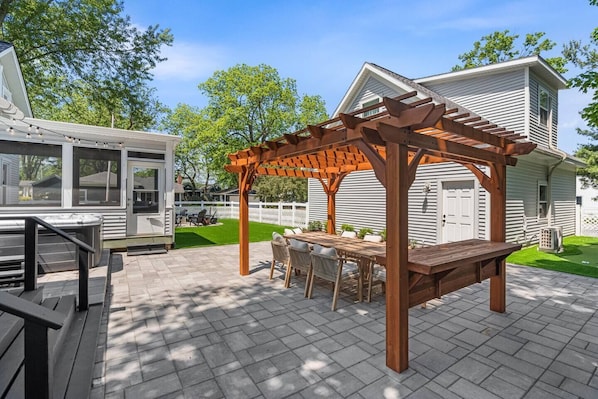 Une terrasse couverte avec une pergola en bois, des sièges d’extérieur et une vue sur une maison.