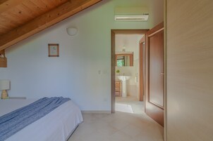 A bedroom with a bed, a bedside lamp, a framed picture on the wall, and an air conditioning unit.