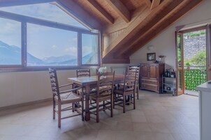 Un comedor con mesa y sillas de madera, ventanas amplias con vista a la montaña, y una zona de cocina con armarios y una planta.