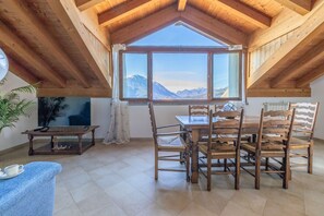 A dining area with a table and chairs, a television, and a view of mountains through a large window. - Il Nido sul Lago in Perledo (Perledo)