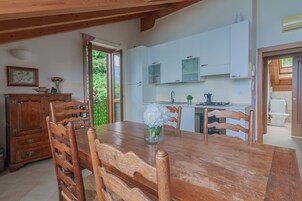 A wooden dining table with chairs, a vase with flowers, and a kitchen with white cabinets and a stove.