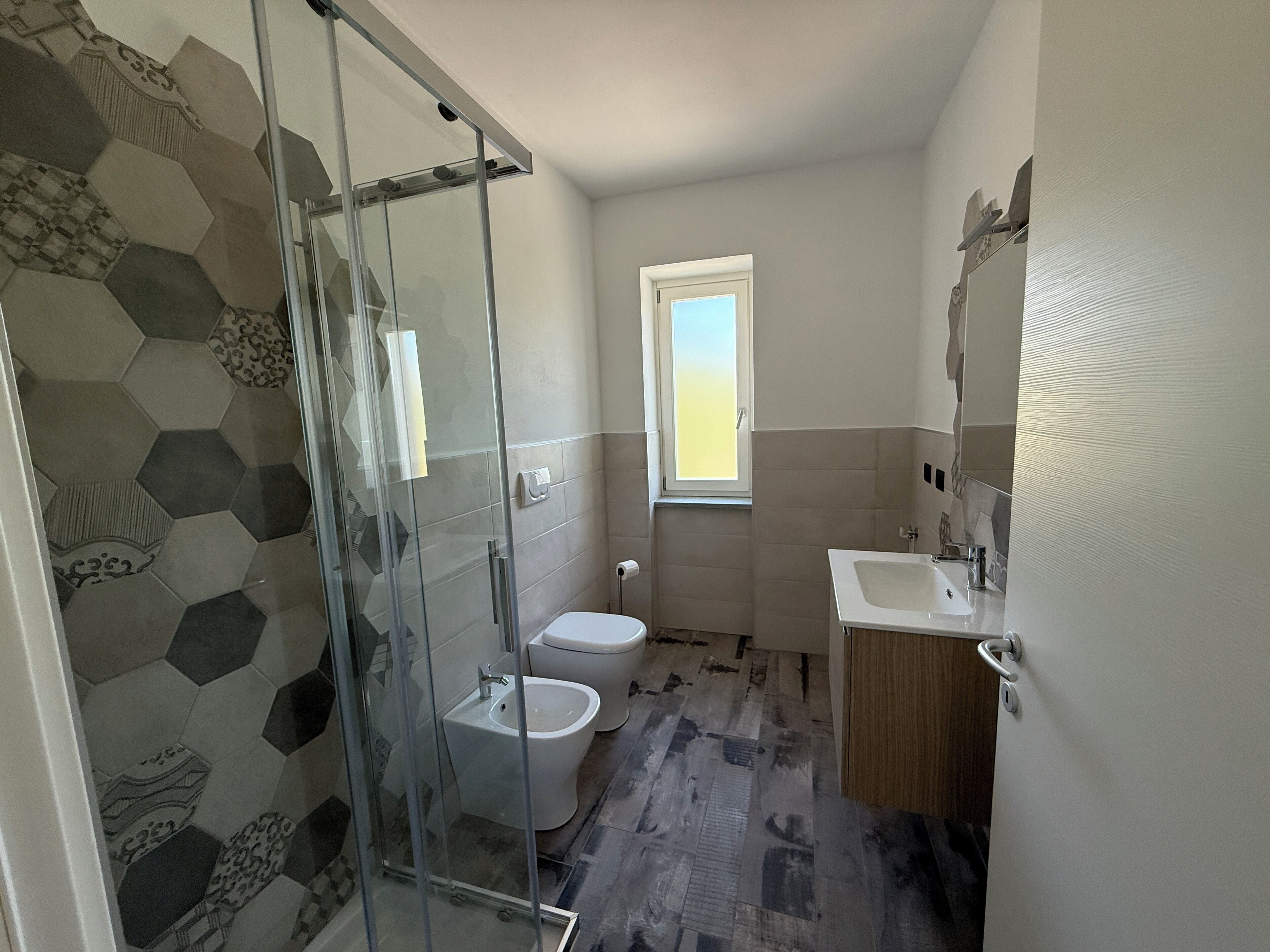 A bathroom with a glass shower enclosure, a toilet, a bidet, and a sink.