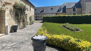 A courtyard with stone buildings, a paved walkway, and well-maintained hedges.