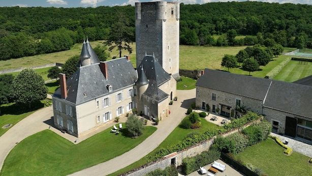 A castle with a prominent tower, surrounded by well-maintained gardens and a tennis court.