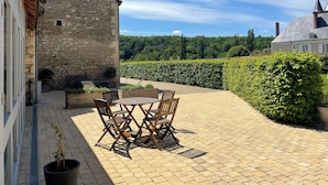 A patio with a table and chairs, stone walls, and a hedge.