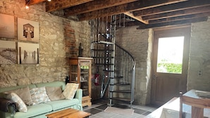 A rustic interior with a stone wall, a spiral staircase, a green sofa, and a wooden table.