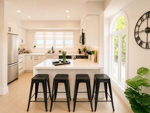 A modern kitchen with a central island, bar stools, and a large clock on the wall.