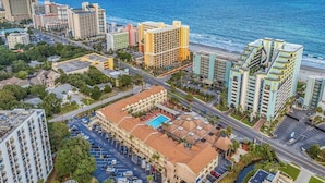 Vista aérea de uma área hoteleira à beira-mar, com vários edifícios, um estacionamento e uma praia.