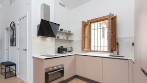 A compact kitchen with a built-in oven, a coffee maker, and a window with wooden shutters. - Mirador de Aixa (Granada)