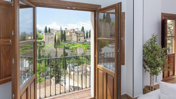 A room with a large sliding glass door leading to a balcony with a view of historic buildings and greenery. - Mirador de Aixa (Granada)