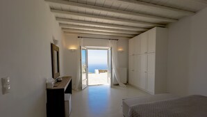 A bedroom with a bed, a wardrobe, a desk, and a view of the sea through an open door. - Villa Prive 88 Mykonos (Mykonos)