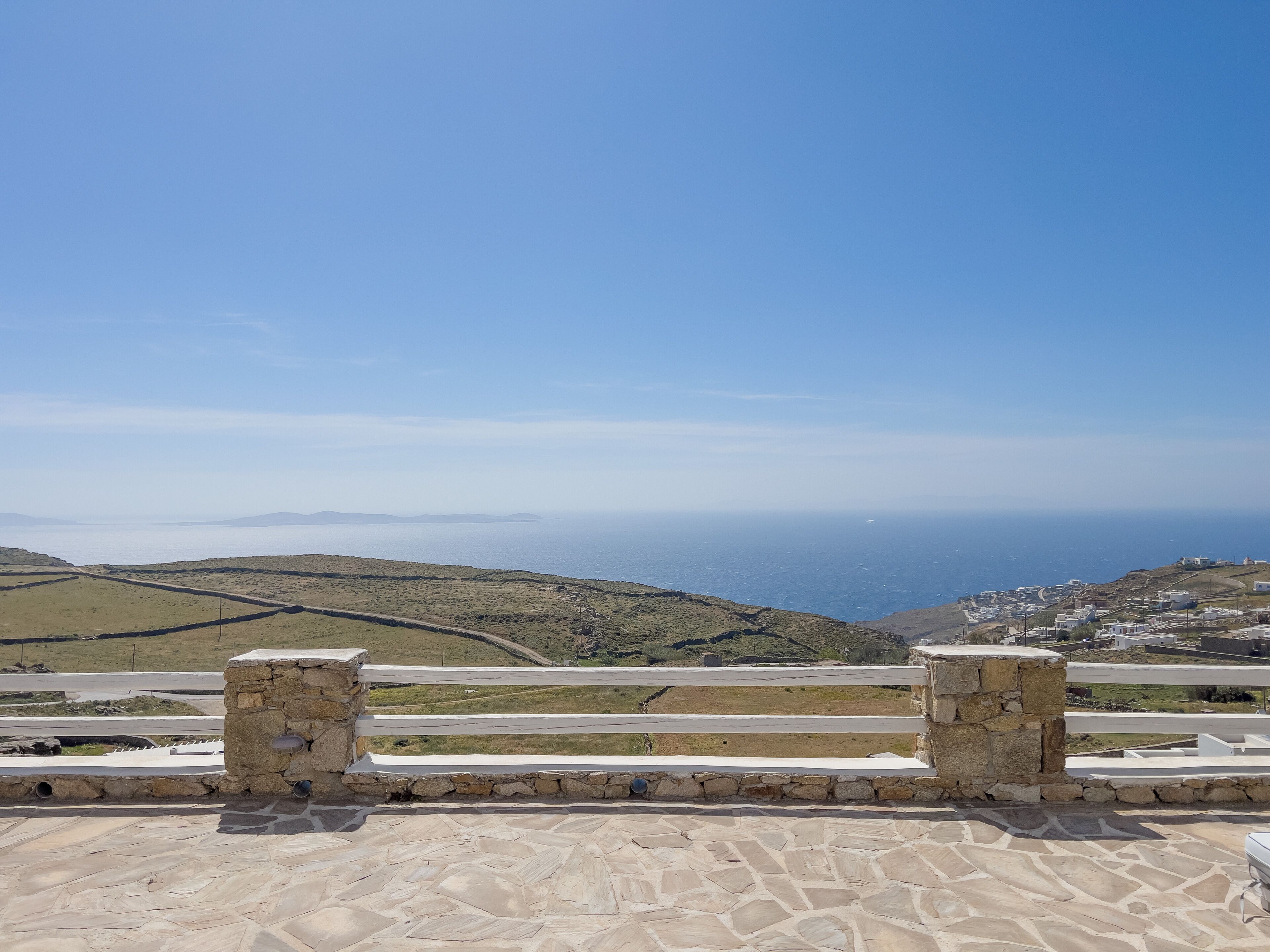 A stone terrace with a view of a coastal landscape, including hills and a distant body of water.
