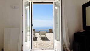 A room with a bed, a radiator, and a view of the sea through an open door. - Villa Prive 88 Mykonos (Mykonos)