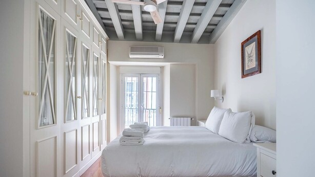 A bedroom with a bed, bedside tables, a wardrobe, an air conditioning unit, and a window. - Otumba 22 House (Sevilla)