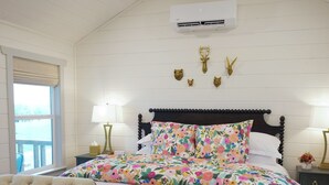Un dormitorio con cama, dos mesitas de noche, ventilador de techo, equipo de aire acondicionado y ventana con vistas.