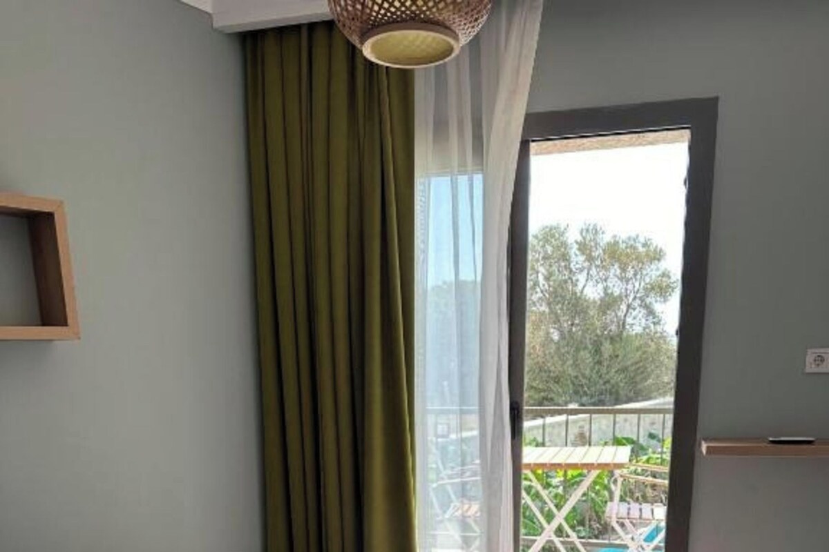 A bedroom with a bed, a window with curtains, and a view of an outdoor area.