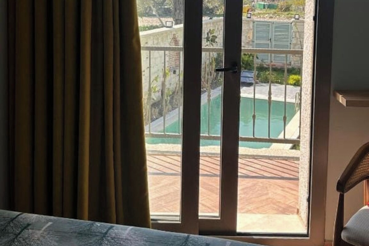 A room with a bed, a chair, and a view of a swimming pool through a sliding glass door.